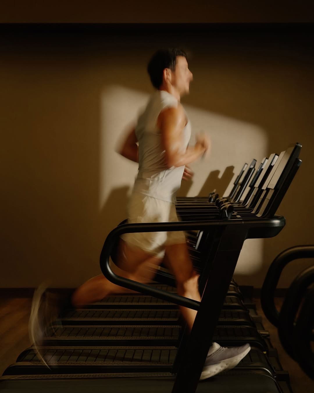 Runner mid-stride on a treadmill in a warm-lit gym